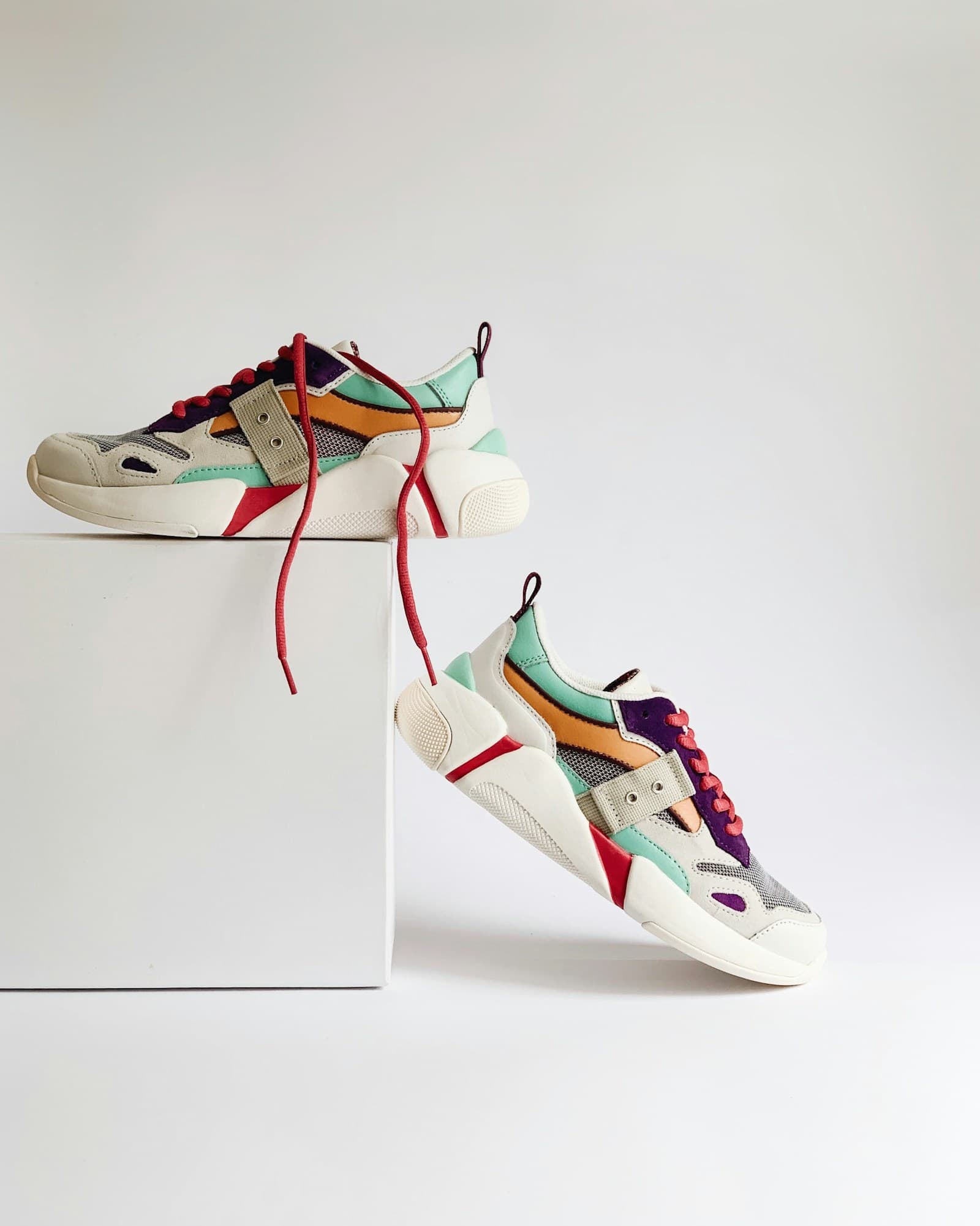 Colorful athletic shoes are displayed on a white background and a cube.