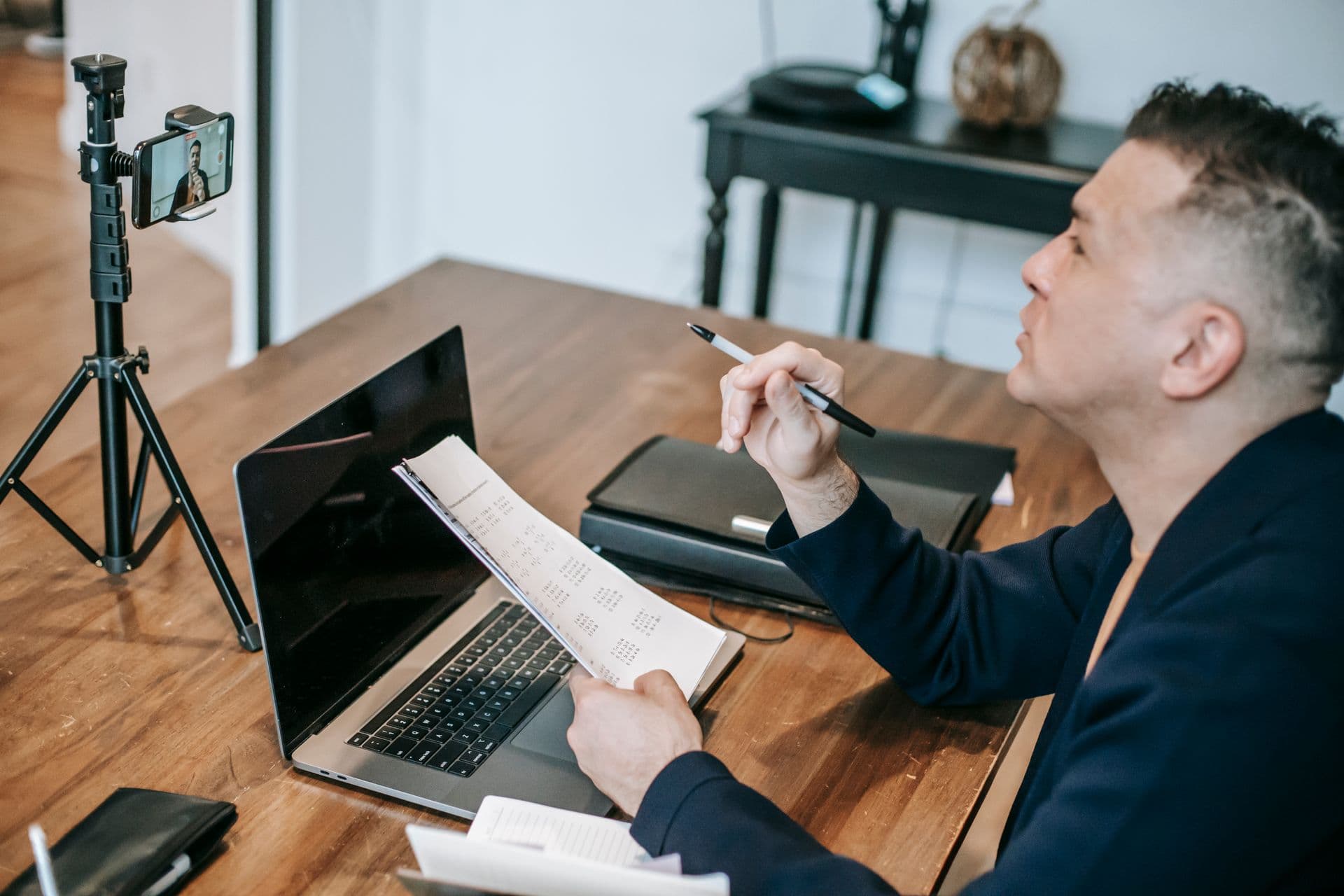 Man at a laptop speaking towards a smartphone on a tripod, illustrative stock photograph of remote teaching