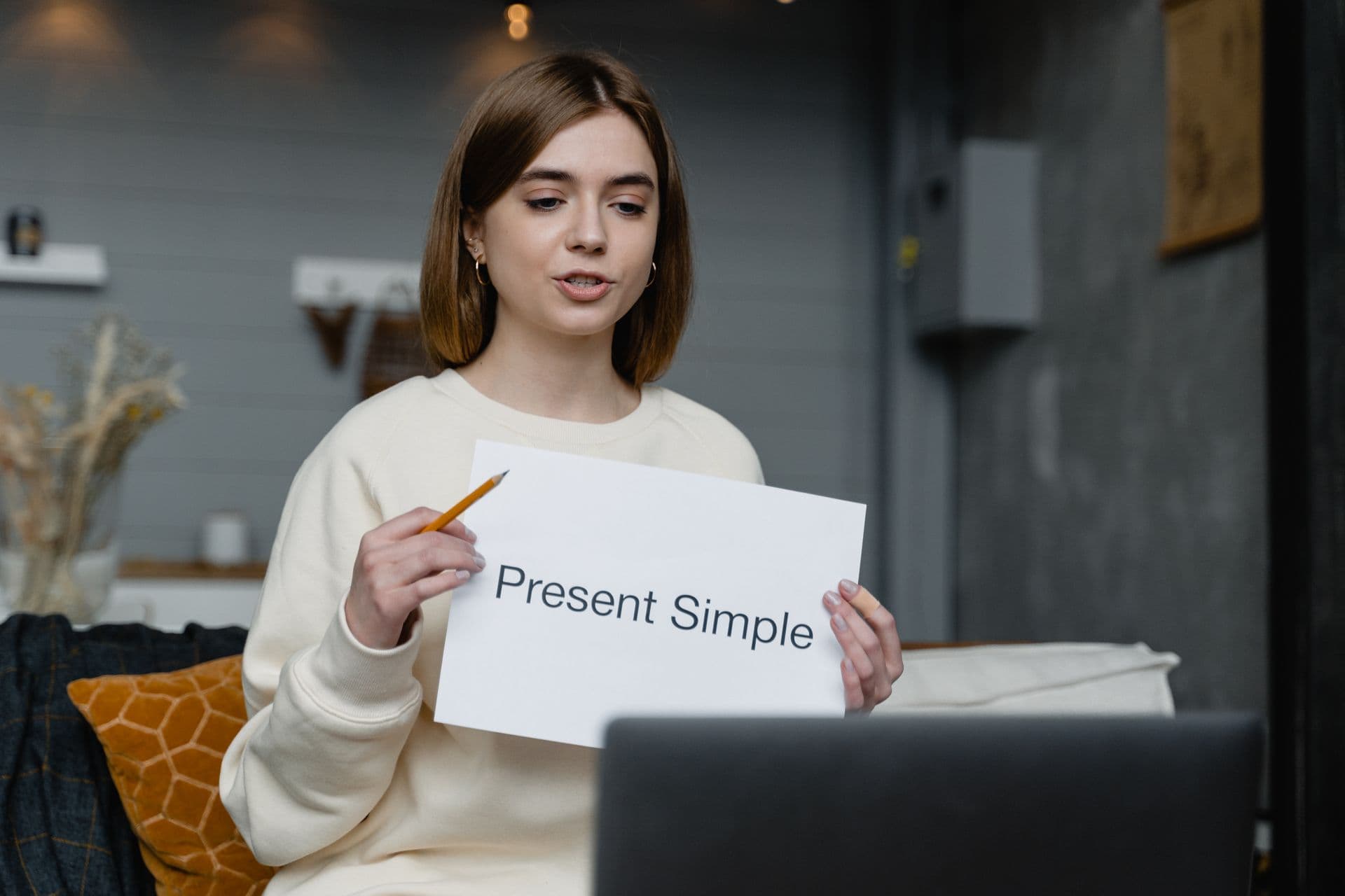Woman teaching at a laptop and holding a Present Simple lesson sheet, illustrative stock photograph